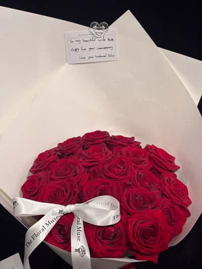Overhead view of a dome of red roses with a handwritten gift card, ivory wrap